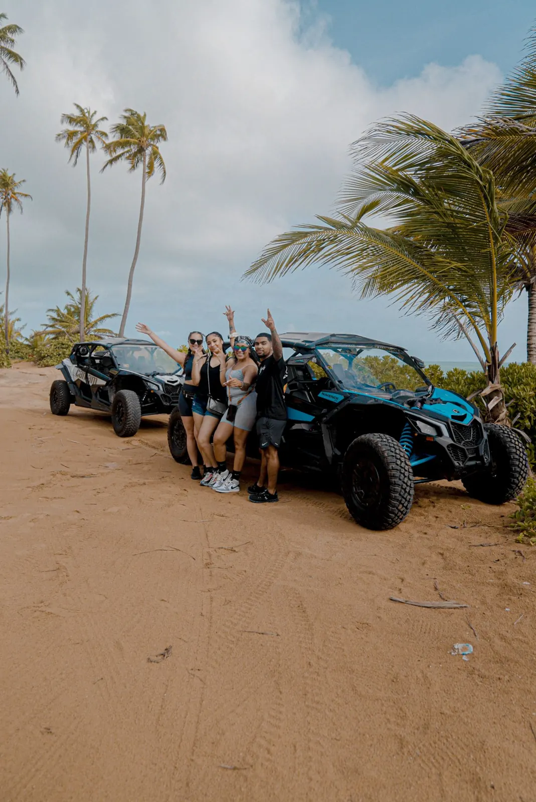 Group of friends celebrating next to their Can-Am on a palm-lined beach trail in Puerto Rico