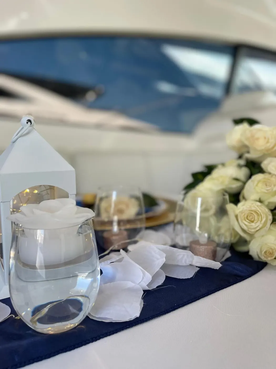 Close-up of white roses lantern and rose petals on navy runner
