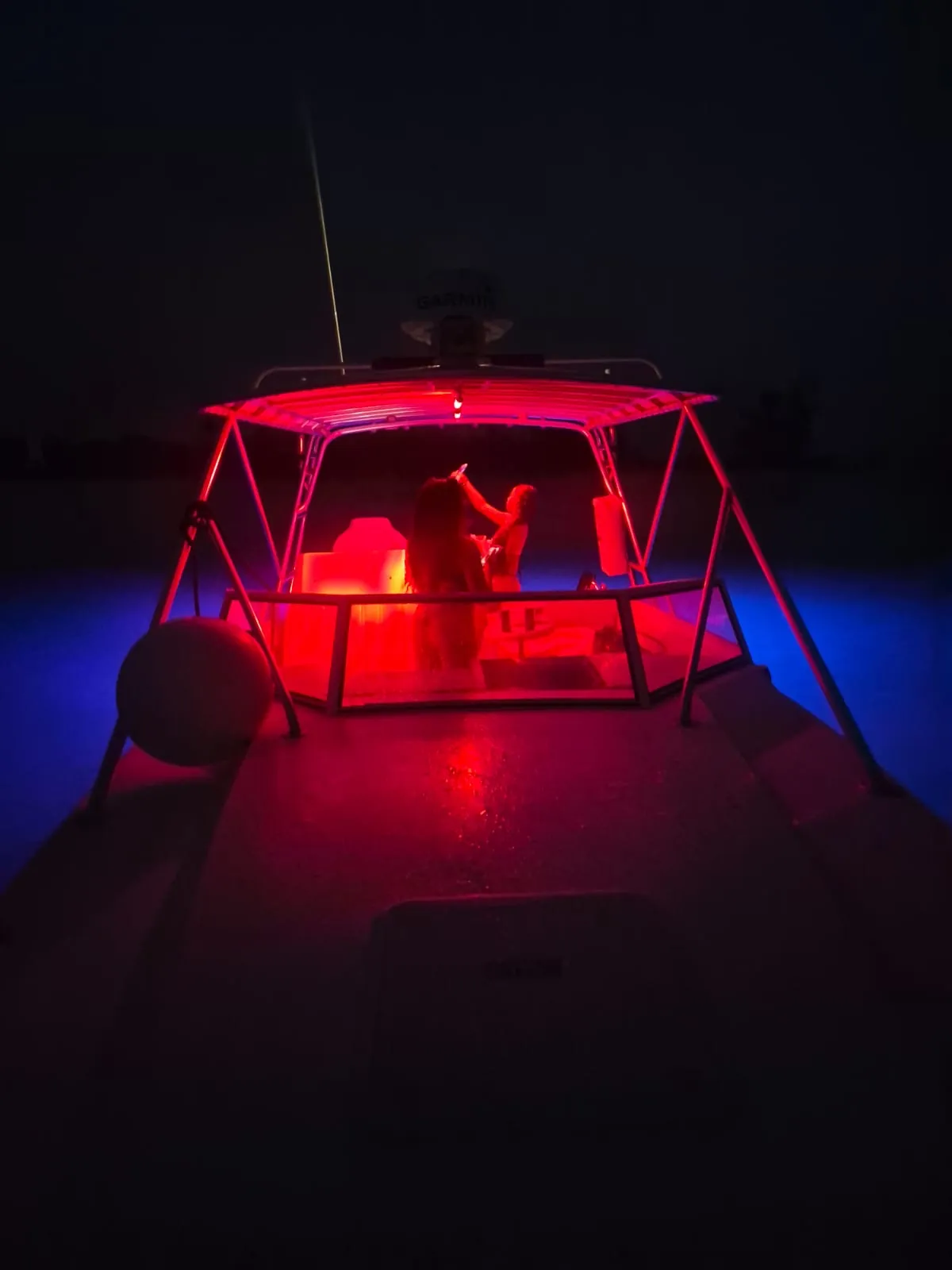 Guests under the red-lit hardtop of the Contender 38 at night with blue underwater lights glowing on either side of the hull