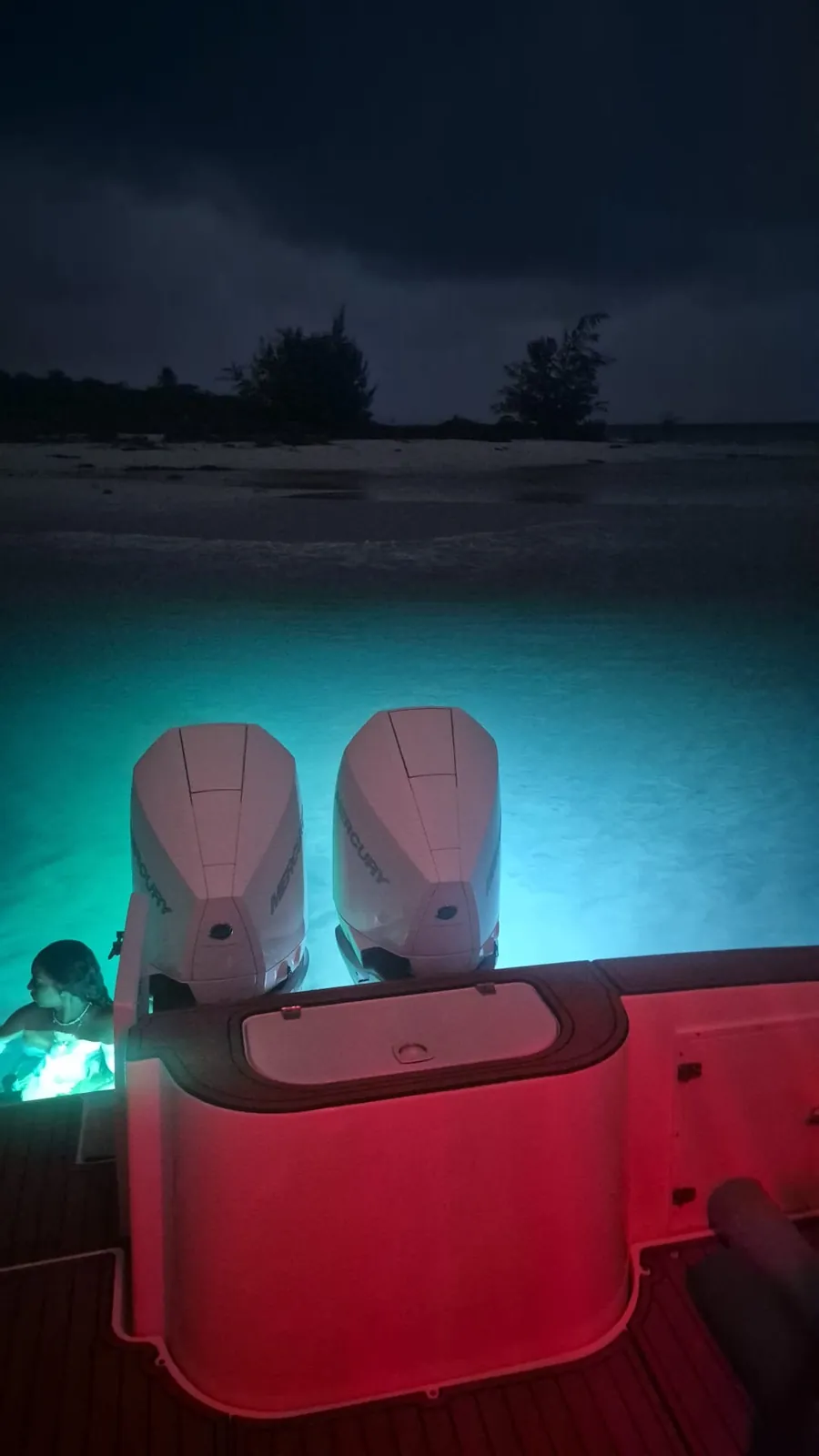 Twin Mercury outboards on the Contender 38 with turquoise underwater lights illuminating the shallow water and a guest swimming beside the boat at Palomino