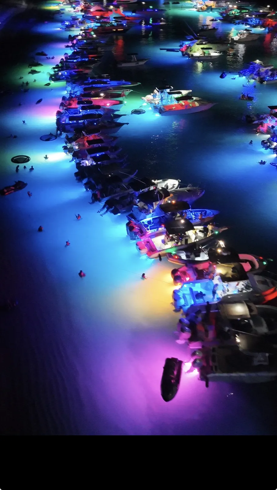 Drone photo of dozens of boats anchored together at night with underwater lights turning the shallow water blue, pink, green and purple off Palomino Island Puerto Rico
