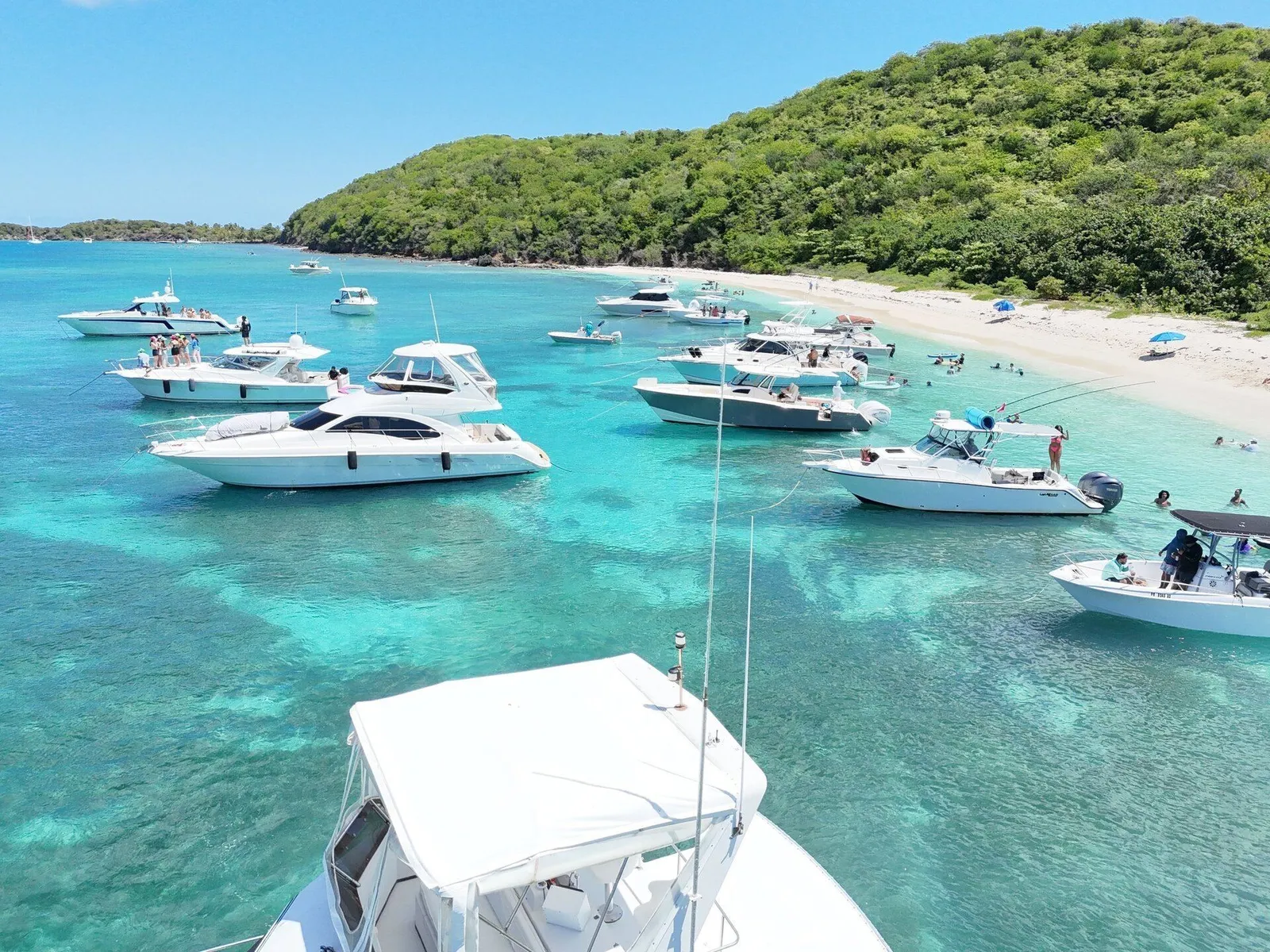 Aerial of multiple charter boats anchored along a Caribbean sandbar with green tropical hill