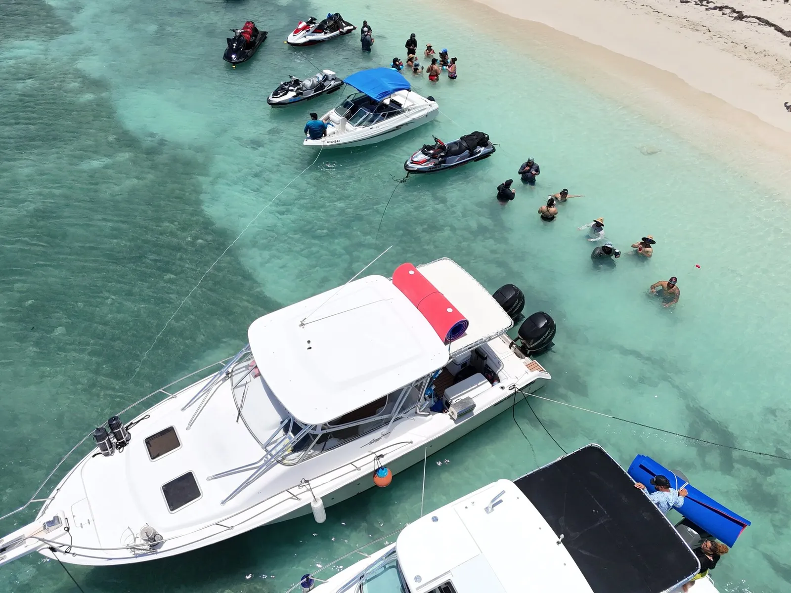 Aerial of busy Caribbean sandbar with jet skis, sport yacht and guests swimming