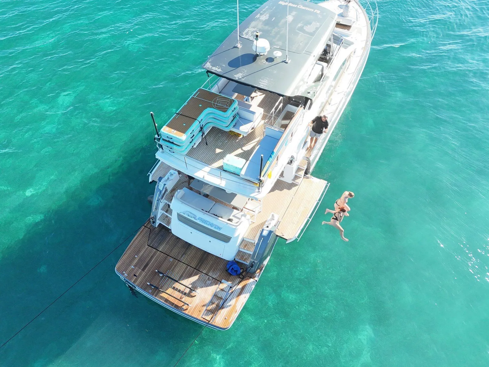 Top-down aerial of luxury yacht with guest jumping off the swim platform into turquoise water